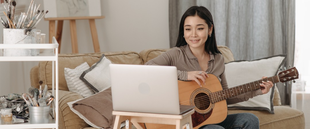 Eine Frau sitzt auf einer Couch und lernt Gitarrespielen