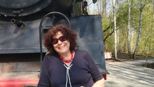 Renate steht im Freizeitoutfit vor einer alten Dampflok und lächelt in die Kamera