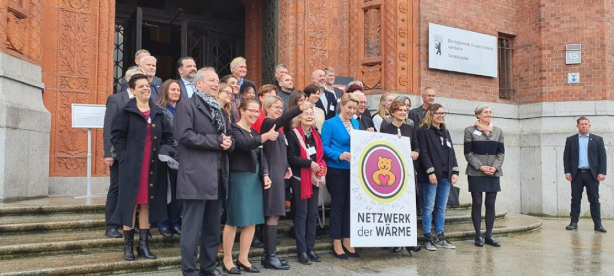 Die Gruppe der Gründer:innen des Netzwerks der Wärme stehen vor der Senatskanzlei und halten das Logo des Projekts in die Luft