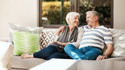 Älteres Ehepaar sitzt auf Couch und lächelt sich an.