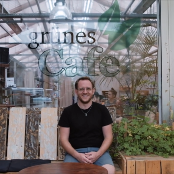Lukas sitzt mit einem stolzen Lächeln auf einer selbstgebauten Holzbank vor dem Grünen Café