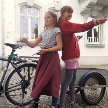 Zwei Mädchen stehen vor einem Lastenrad und verteilen Flyer.