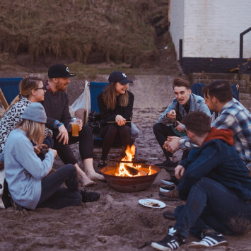Junge Menschen sitzen im Kreis um Lagerfeuer, eine Person redet.