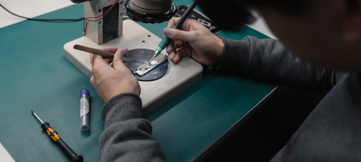 Person repariert Gegenstand unter Mikroskop mit Werkzeug