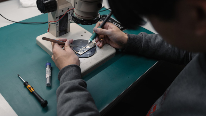 Person repariert Gegenstand unter Mikroskop mit Werkzeug