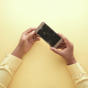 Zwei Hände halten zersprungenes Smartphone vor gelbem Hintergrund