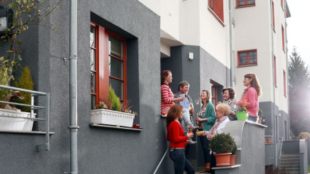 Nachbar:innen stehen gemeinsam bei einem Getränk vor einem Hauseingang und unterhalten sich
