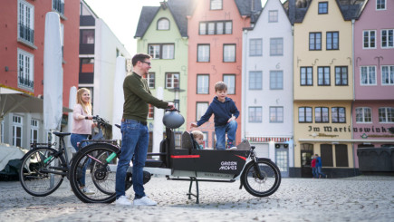 Mit dem E-Lastenrad transportiert ein Vater seine Kinder ber den gepflasterten Marktplatz. Seine Frau hat ein E-Bike gewählt