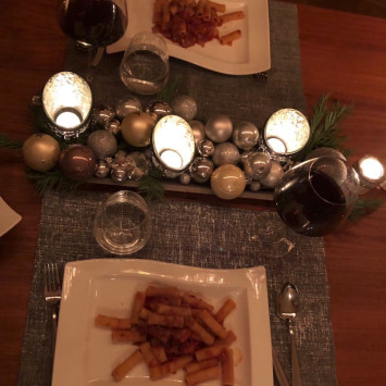 Weihnachtlich gedeckter Tisch mit zwei Tellern Pasta Arrabiata und zwei Gläsern Rotwein