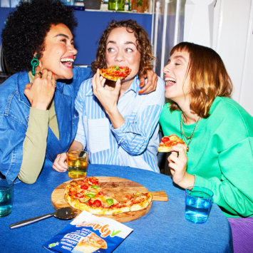 Drei Freund:innen verspeisen lachend eine Pizza mit dem simplyV Pizzakäse