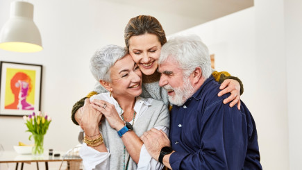 Drei Personen umarmen sich, die zwei Senior:innen im Vordergrund tragen die Patronus-Uhr und freuen sich über das neue Gefühl der Sicherheit