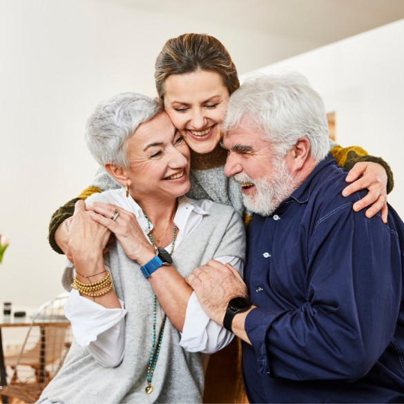 Drei Personen umarmen sich, die zwei Senior:innen im Vordergrund tragen die Patronus-Uhr und freuen sich über das neue Gefühl der Sicherheit