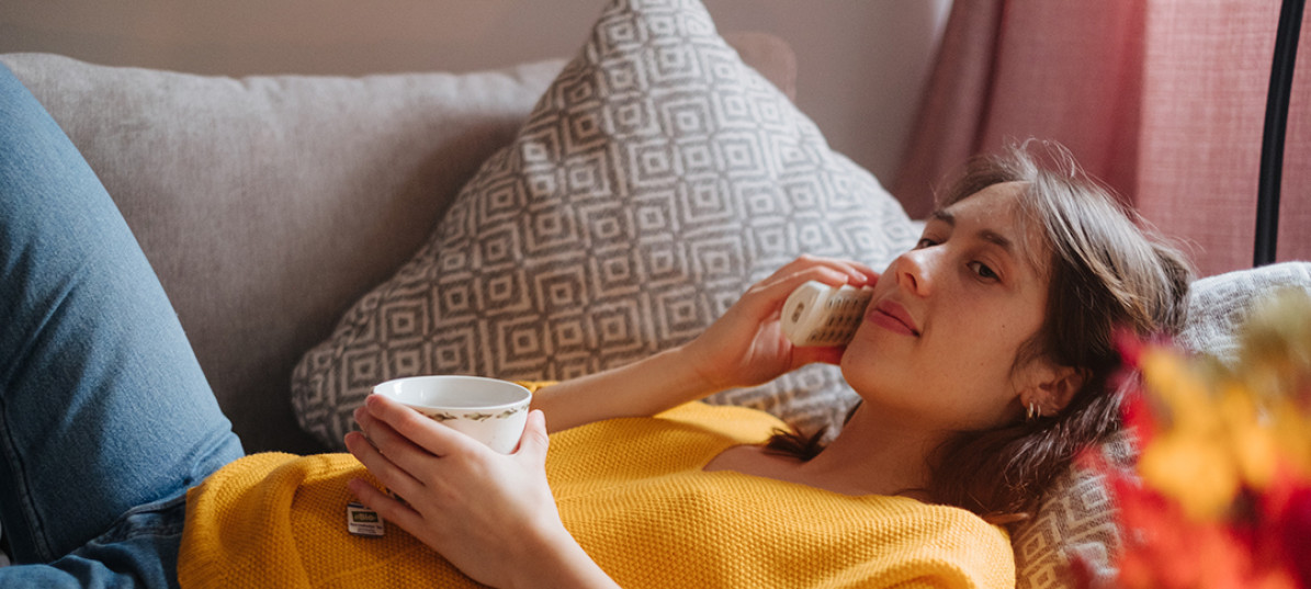 Eine Frau liegt mit einer Tasse Tee auf der Couch und telefoniert