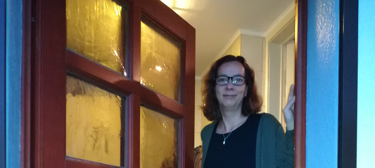 Anja aus Berlin steht lächelnd an ihrer geöffneten Haustür