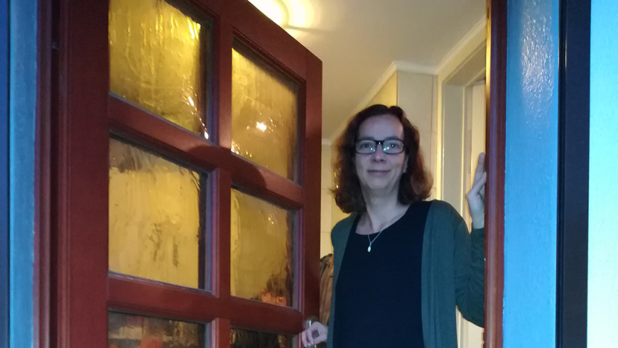 Anja aus Berlin steht lächelnd an ihrer geöffneten Haustür