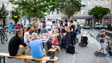 Eine Gruppe von Menschen sitzt auf einem Platz zusammen und feiert ein Straßenfest.