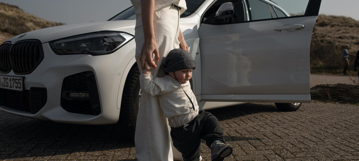 Baby läuft an den Händen einer Frau vor einem weißen Auto