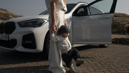 Baby läuft an den Händen einer Frau vor einem weißen Auto